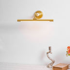 Lit against a plain wall, this Clérachic wall sconce in gold sits above a styled tablescape with a candlestick and open book.