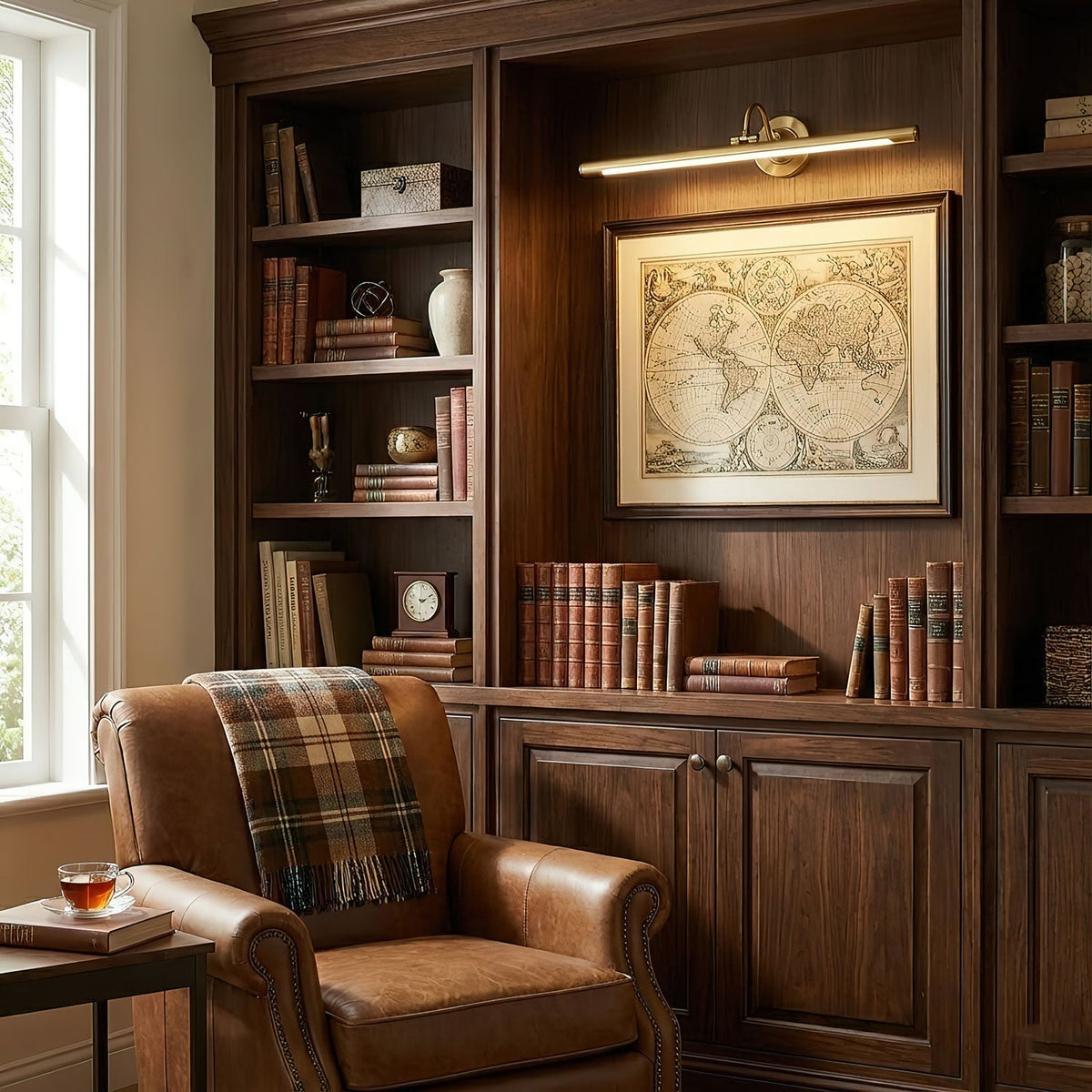 In a built-in bookshelf library, this Clérachic wall sconce in gold lights a framed map above a leather armchair.