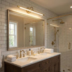 Above a double vanity in a bathroom with white subway tile, this gold Clérachic wall sconce lights the mirror.