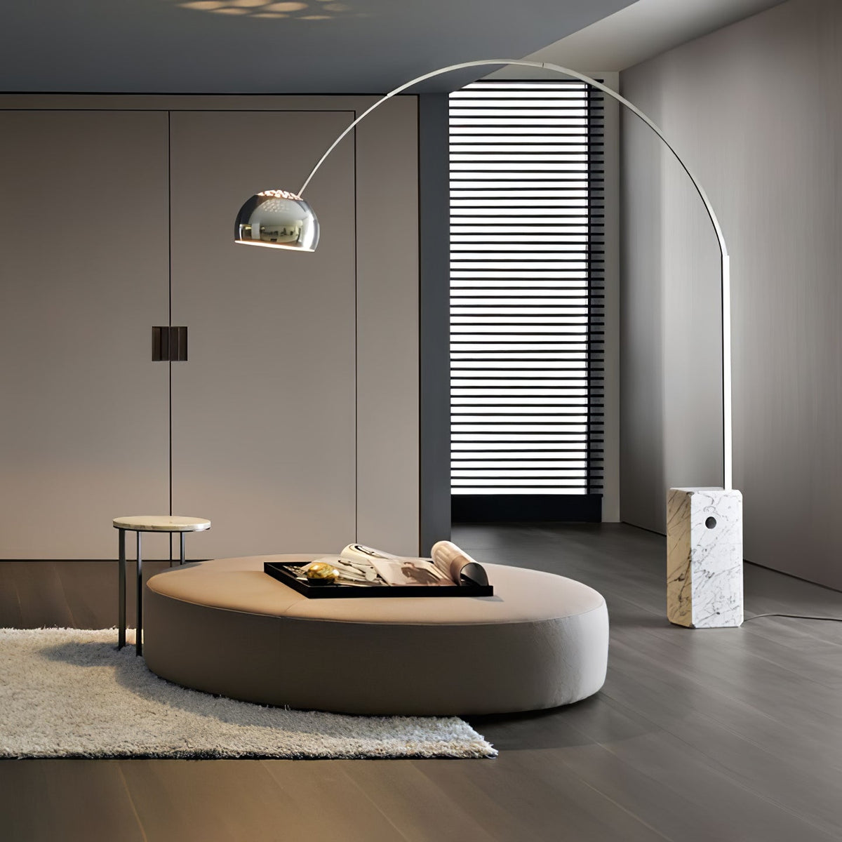 The Clérachic arc lamp's chrome dome glows softly above a round taupe ottoman styled with a tray, set on a plush grey rug.