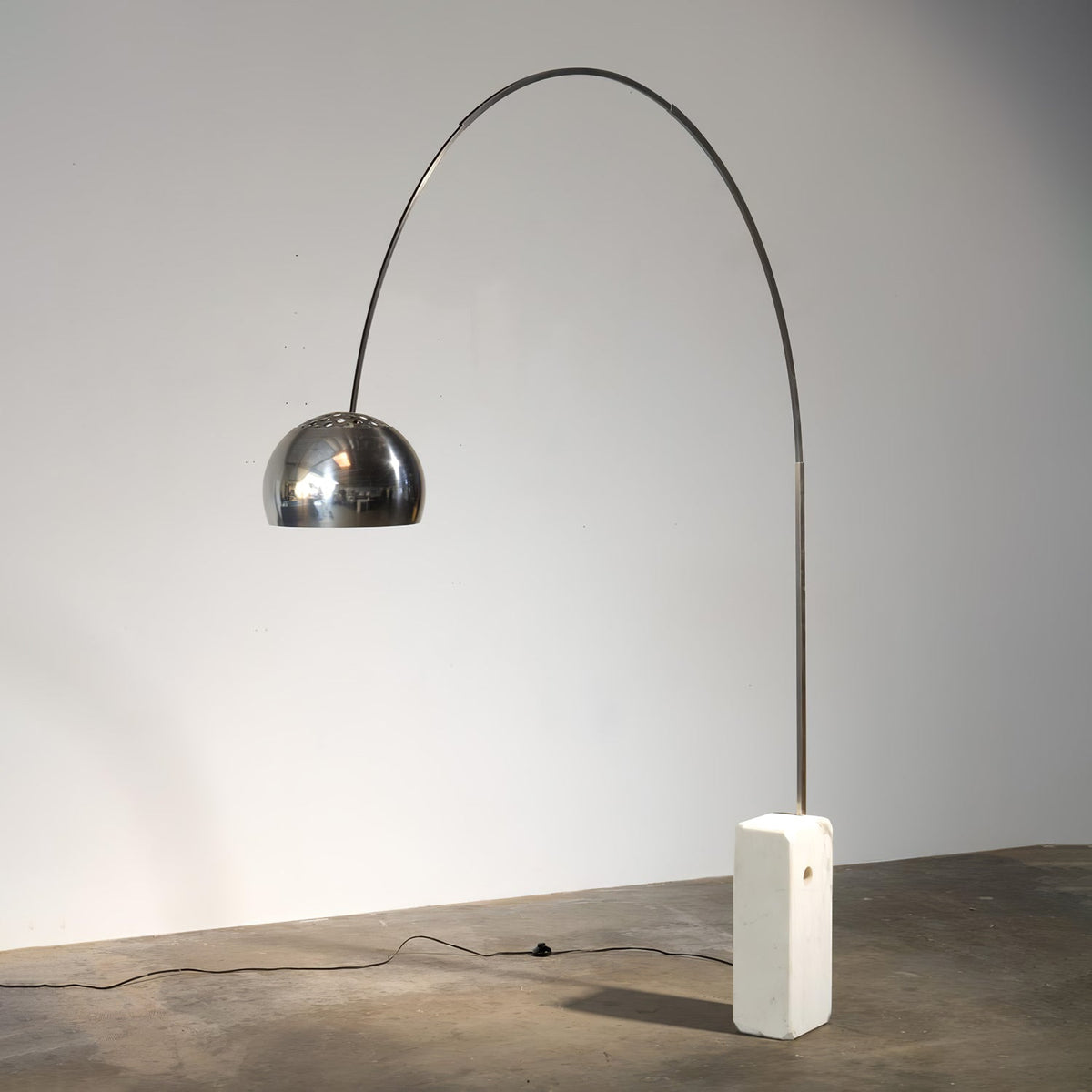 A Clérachic arc floor lamp shown alone against a plain grey backdrop, its full steel arch and chrome dome clearly in view.