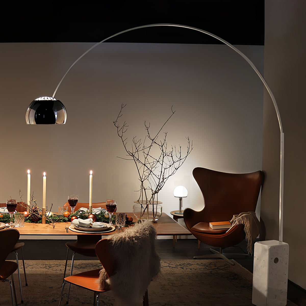 Candlelight and the Clérachic arc lamp's dome light a dressed dinner table, with a leather egg chair and faux fur throw nearby.