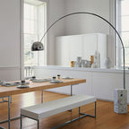 The Clérachic arc lamp's chrome dome hangs above a long wooden dining table with bench seating and a white ceramic sideboard.