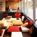 In a retro chalet-style lounge, the Clérachic arc lamp's marble base stands among floor cushions, a red chair and a guitar.