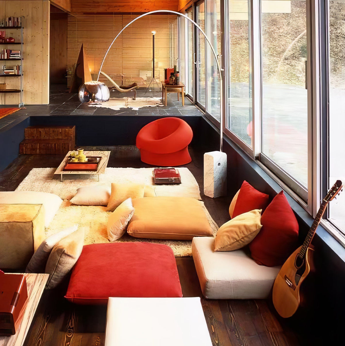 In a retro chalet-style lounge, the Clérachic arc lamp's marble base stands among floor cushions, a red chair and a guitar.