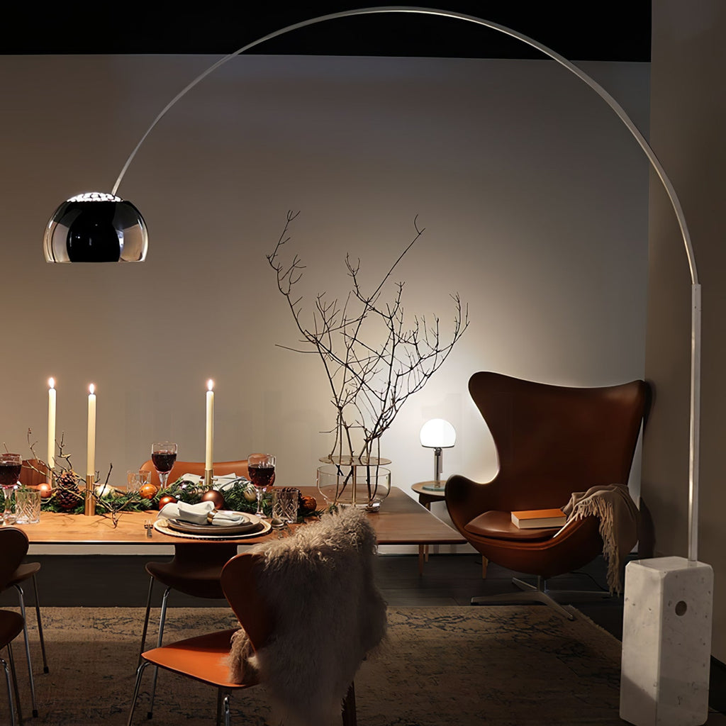 A second view of the candlelit dinner table shows the Clérachic arc lamp's dome glowing beside the leather egg chair.
