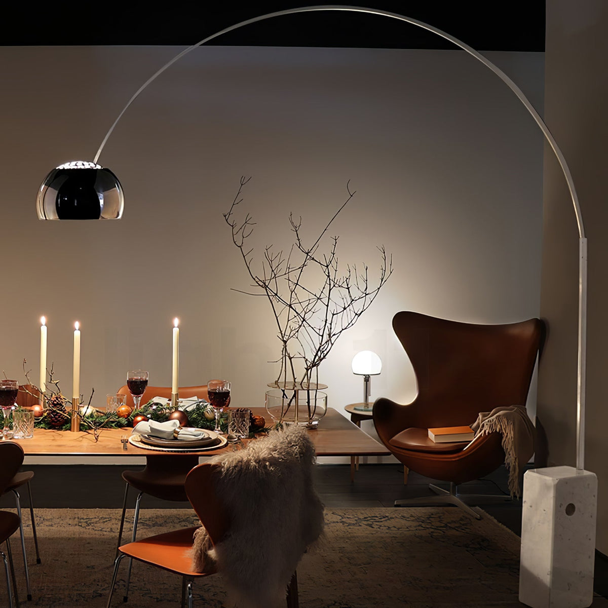 A second view of the candlelit dinner table shows the Clérachic arc lamp's dome glowing beside the leather egg chair.