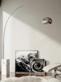 The Clérachic arc lamp's marble base stands beside black-and-white framed art prints and a sheepskin rug on a chaise.