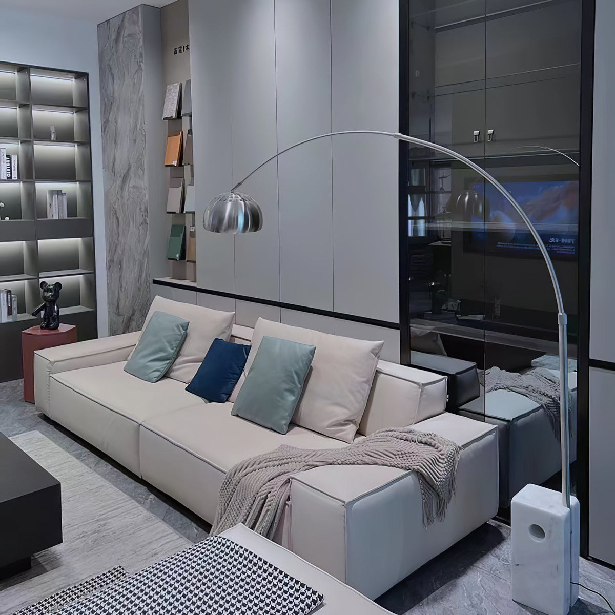 The Clérachic arc lamp's chrome dome is shown close against a two-tone wall, its marble base beside a black leather sofa.