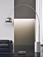 The Clérachic arc lamp's chrome dome arches above a mustard leather sofa and a striped cushion on a black leather sectional.