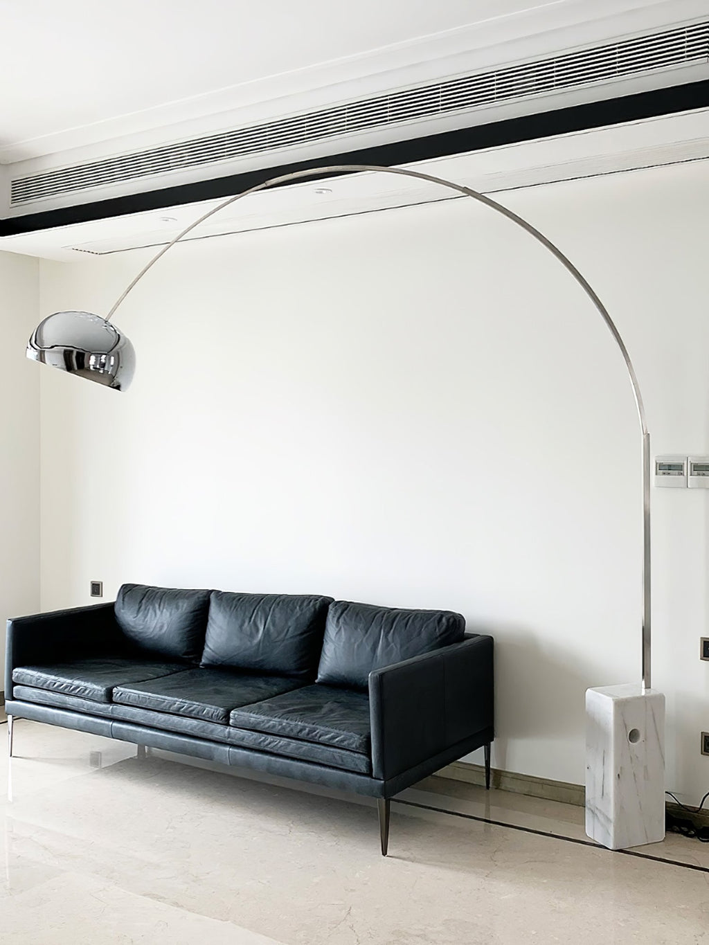 The Clérachic arc lamp curves above a grey sectional sofa, its marble base beside a slim wire-frame side table by the window.