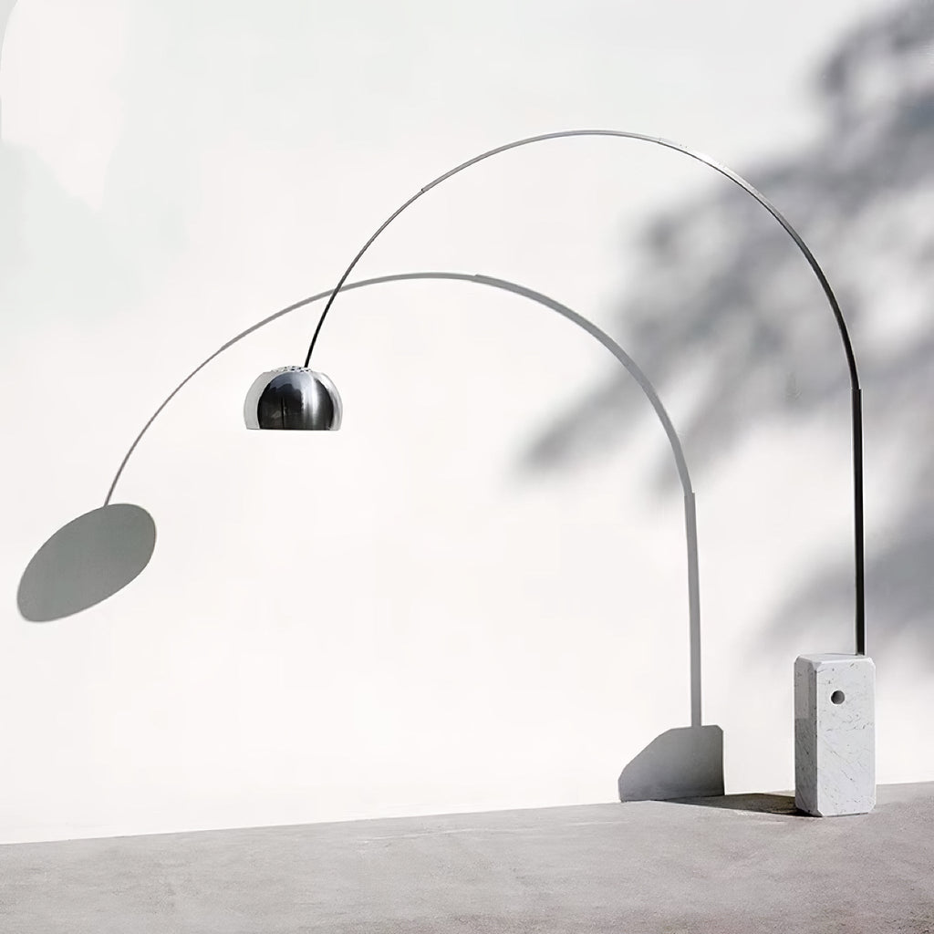 A styled shot casts the Clérachic arc lamp's shadow across a plain wall, its chrome dome and marble base lit from the side.