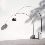 A styled shot casts the Clérachic arc lamp's shadow across a plain wall, its chrome dome and marble base lit from the side.