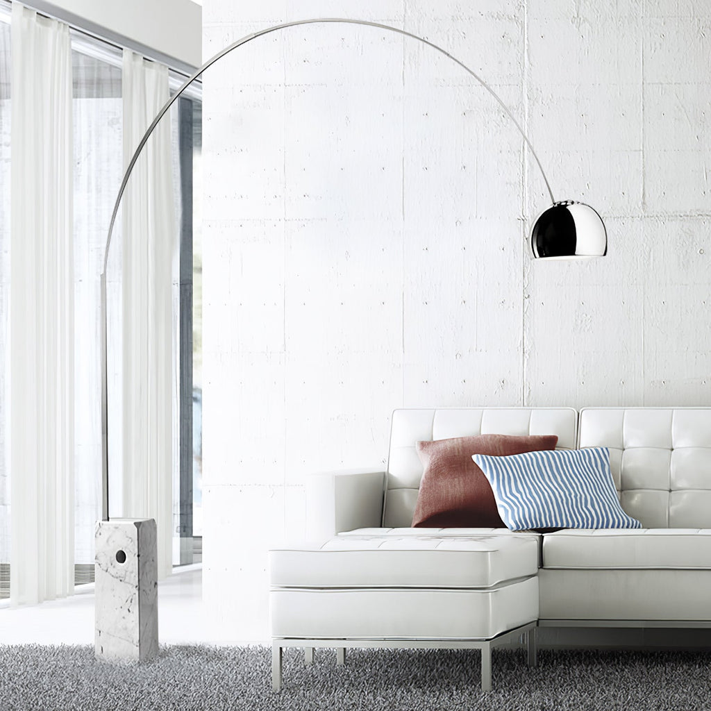The Clérachic arc lamp's chrome dome curves above a white leather sectional sofa with rust and blue striped cushions.