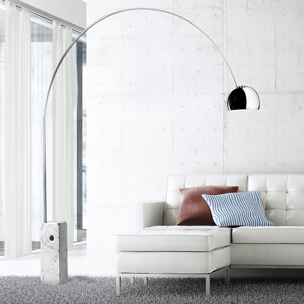 The Clérachic arc lamp's chrome dome curves above a white leather sectional sofa with rust and blue striped cushions.