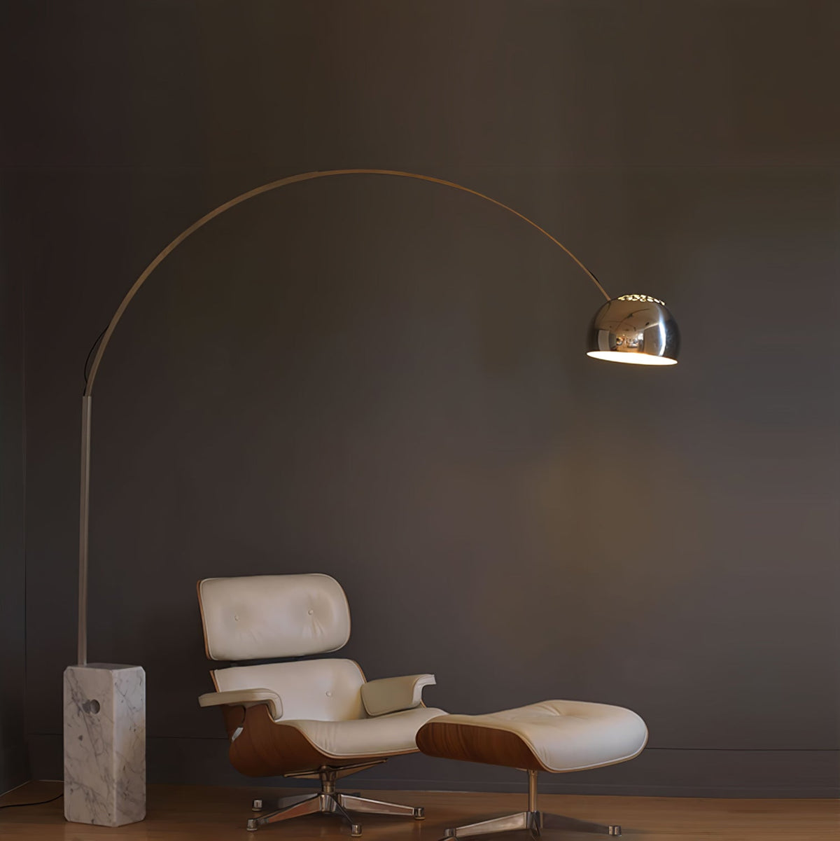 The Clérachic arc lamp's lit chrome dome glows beside a cream leather Eames-style lounge chair and matching ottoman.