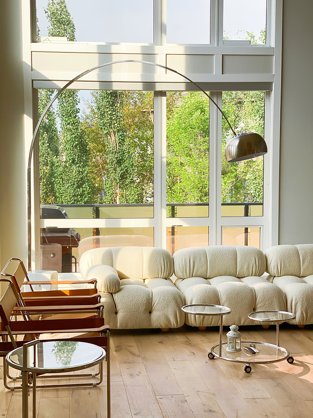 Morning light fills the room as the Clérachic arc lamp's chrome dome arches above a cream bouclé pebble-shaped sofa.
