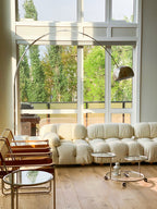 Morning light fills the room as the Clérachic arc lamp's chrome dome arches above a cream bouclé pebble-shaped sofa.