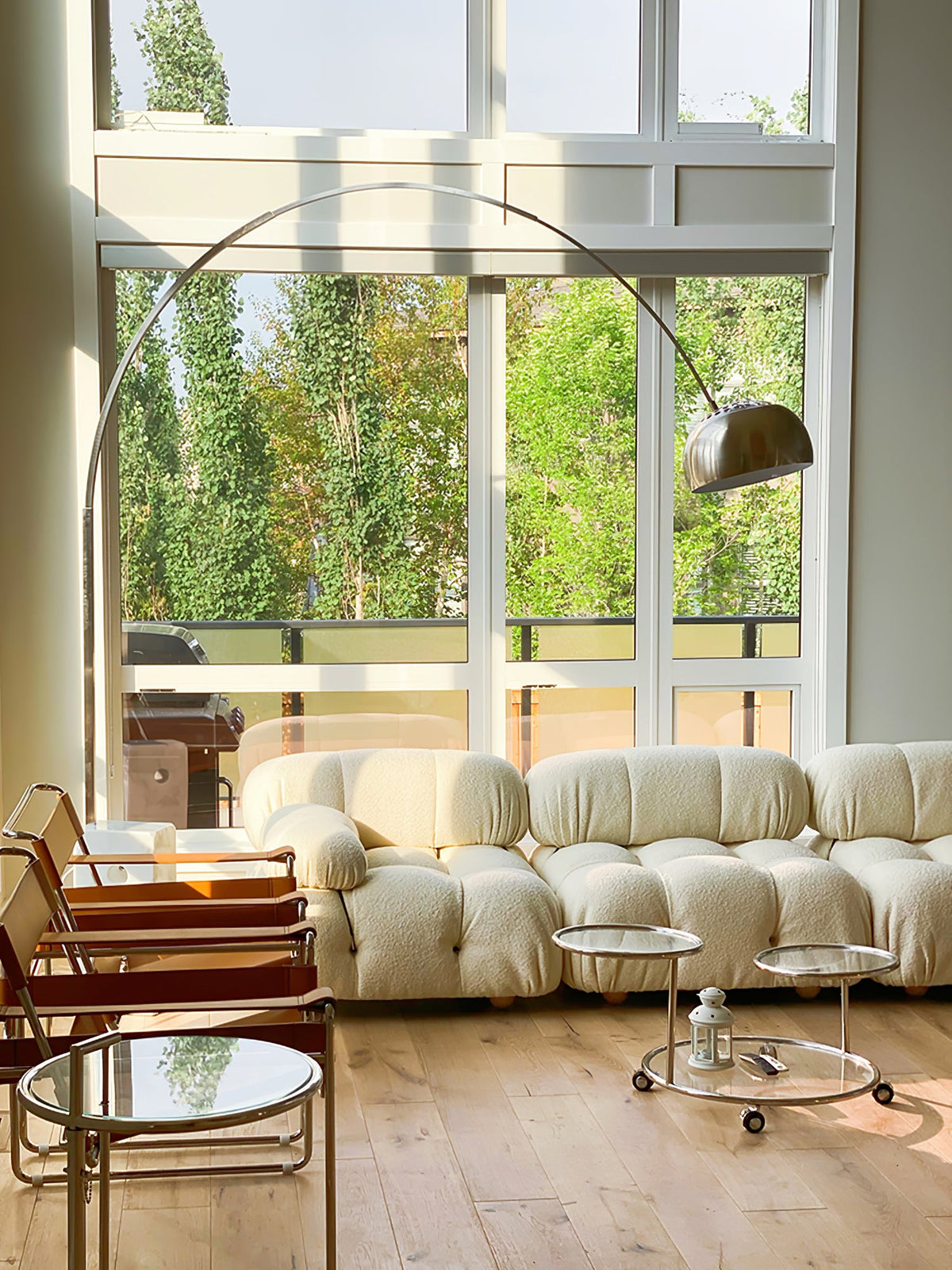 Morning light fills the room as the Clérachic arc lamp's chrome dome arches above a cream bouclé pebble-shaped sofa.