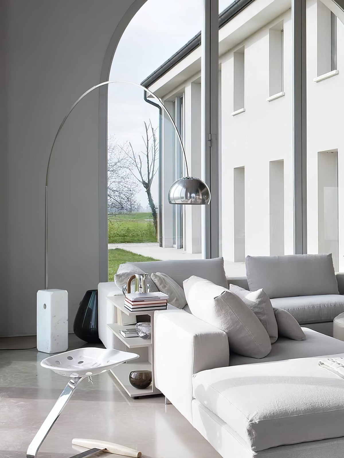 Through an arched doorway, the Clérachic arc lamp's marble base sits beside a light grey sofa and a small shelving unit.
