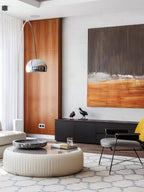 The Clérachic arc lamp's chrome dome curves past a walnut panel wall, its marble base near a black sideboard with bird figures.