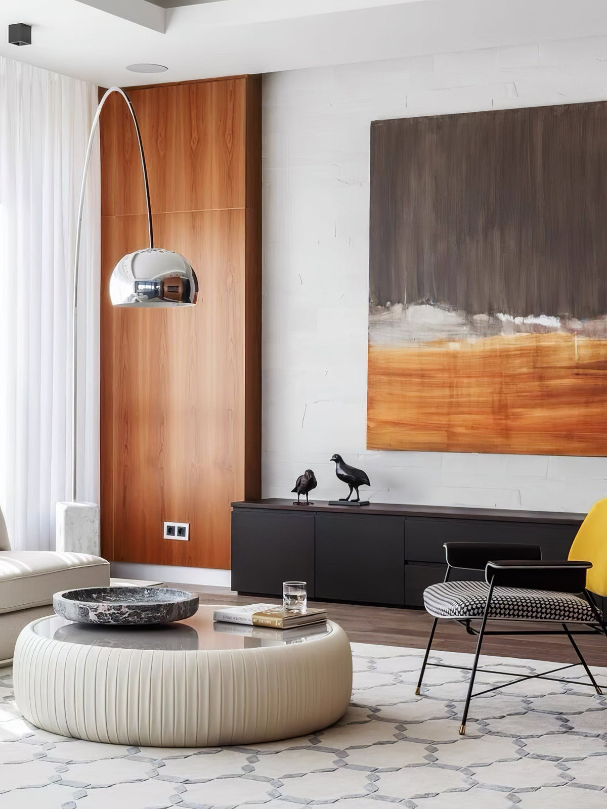 The Clérachic arc lamp's chrome dome curves past a walnut panel wall, its marble base near a black sideboard with bird figures.