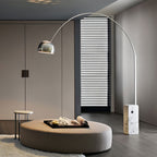 Arc floor lamp with a chrome dome shade curving over a rounded taupe ottoman, its Clérachic marble base by a striped wardrobe.