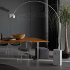 In a dark chalkboard-walled dining room, the Clérachic arc lamp's marble base sits beside a wooden table and potted palm.
