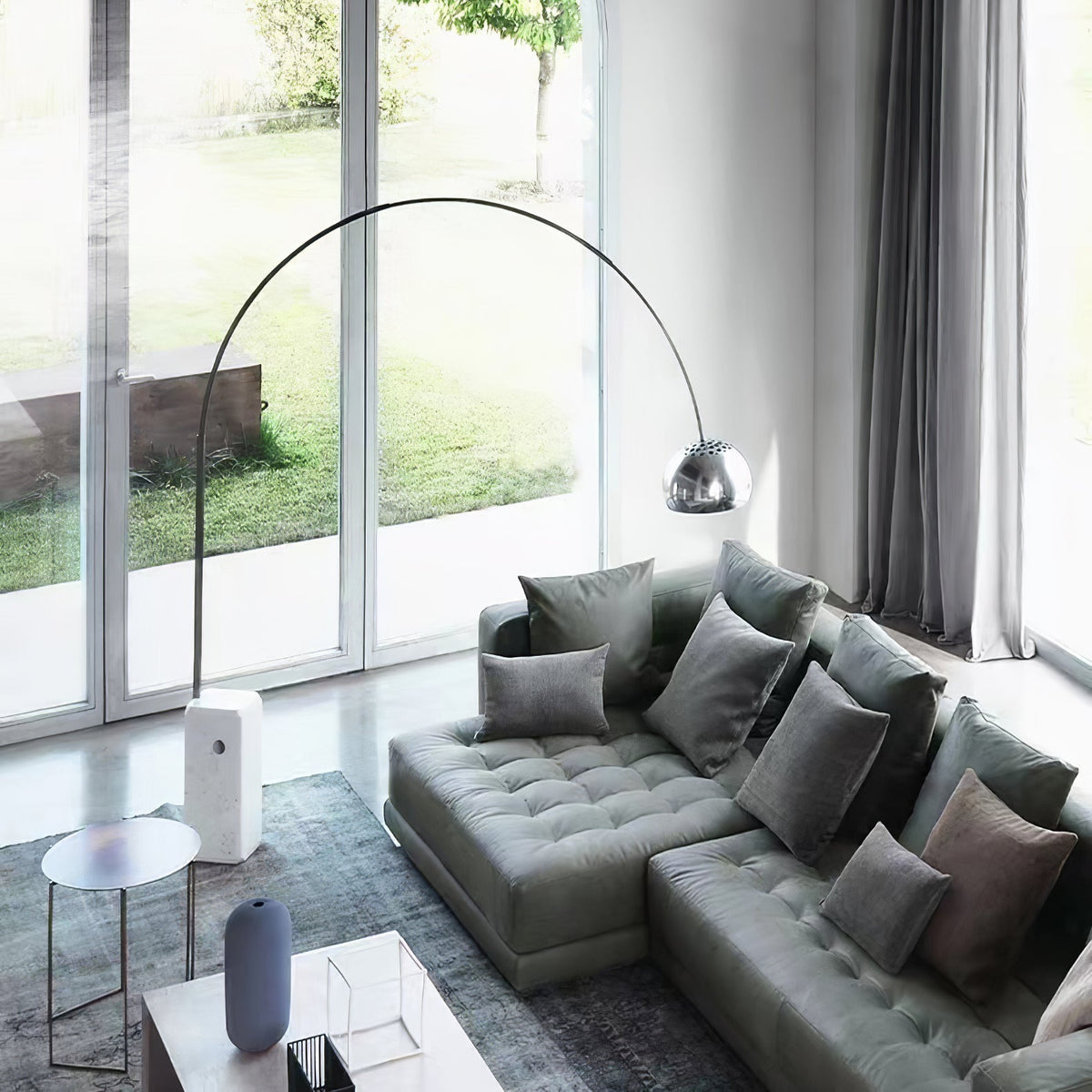 Seen from above, the Clérachic arc lamp's marble base stands by a sage-green sectional sofa facing glass garden doors.