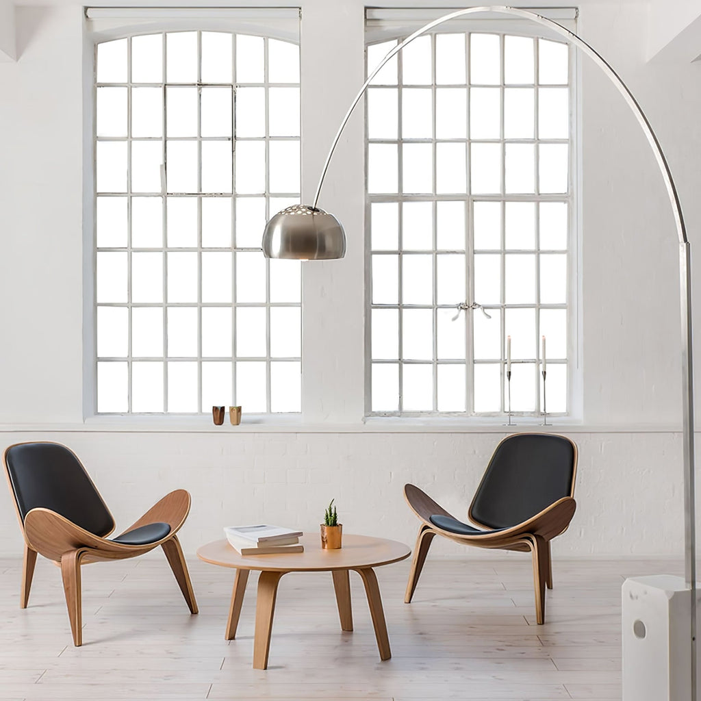 In an industrial loft with steel-framed windows, the Clérachic arc lamp curves above two curved wooden shell chairs.
