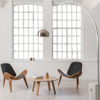 In an industrial loft with steel-framed windows, the Clérachic arc lamp curves above two curved wooden shell chairs.