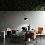 Beneath a living green wall, the Clérachic arc lamp's dome hangs above a dark oval table set with pink leather chairs.