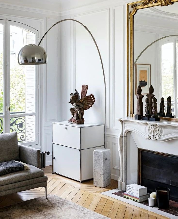 In a Parisian panelled room, the Clérachic lamp's slender steel arch curves past a gilt mirror toward a marble fireplace.