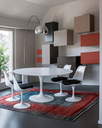A Clérachic arc floor lamp curves over a round dining table and black chairs, its marble base standing against colourful box shelving.