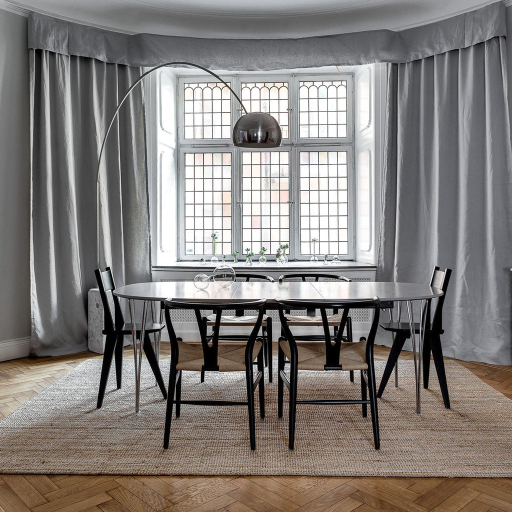 Clérachic's arcing lamp reaches across a bay window, its chrome dome centred above an oval dining table with black wishbone chairs.