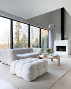 The Clérachic arc lamp's marble base sits beside a chunky white bouclé sofa, chrome dome catching light from a wooded window view.