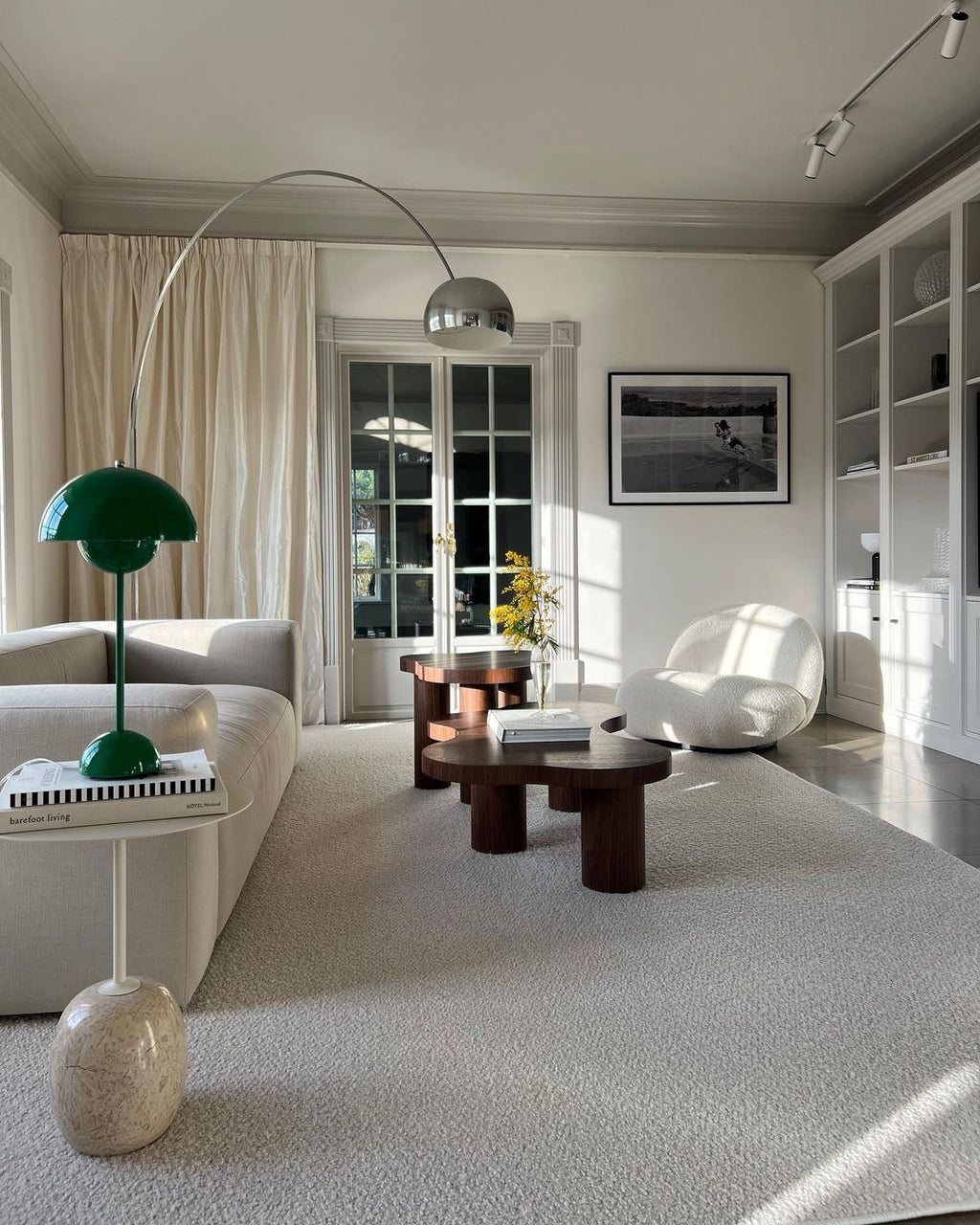 A green table lamp sits nearby as the Clérachic arc lamp's chrome dome arches above two beige armchairs and a dark side table.