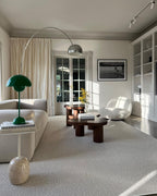 A green table lamp sits nearby as the Clérachic arc lamp's chrome dome arches above two beige armchairs and a dark side table.