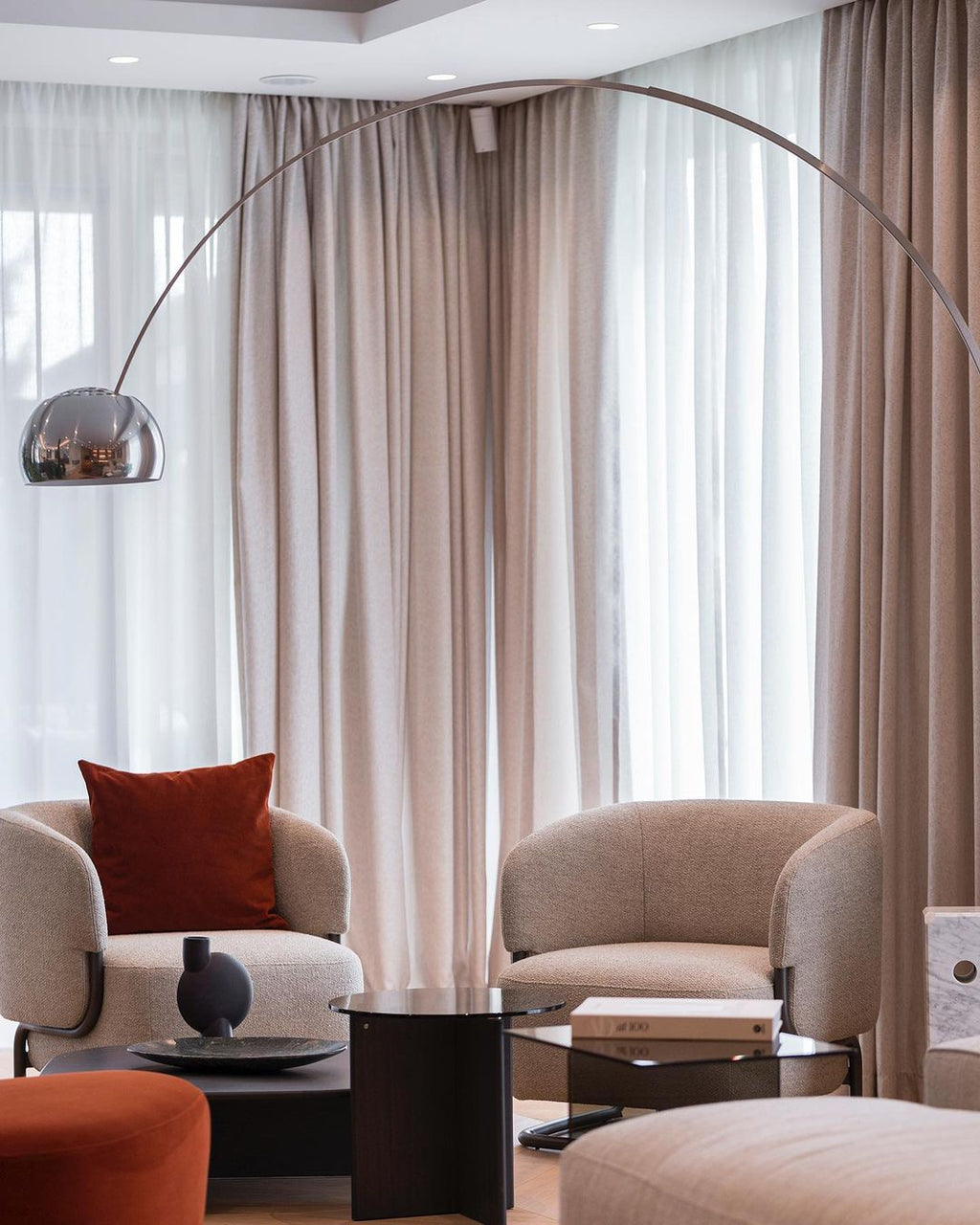 The Clérachic lamp's chrome dome curves above a pair of cream armchairs, a rust cushion and pouf adding warmth to the corner.