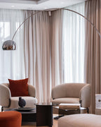 The Clérachic lamp's chrome dome curves above a pair of cream armchairs, a rust cushion and pouf adding warmth to the corner.