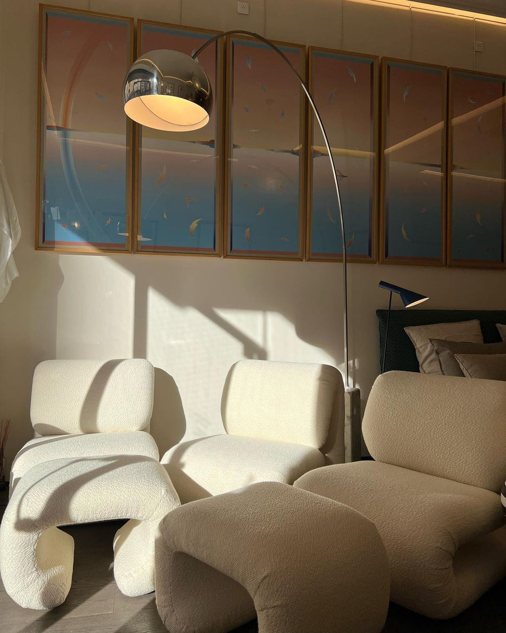 Lit warmly, the Clérachic arc lamp's dome glows over a bouclé armchair and matching ottomans in a dim evening living room.