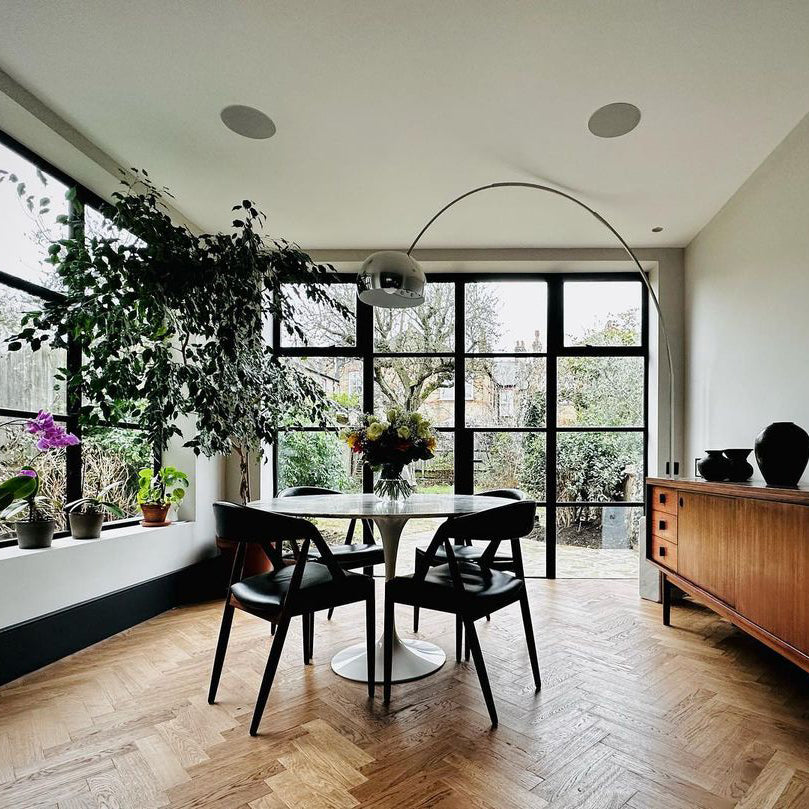 The Clérachic arc lamp curves above a marble dining table and black leather chairs, framed by tall steel-mullioned windows.