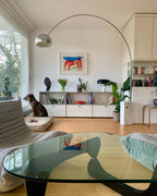 A dog rests on its bed beneath the Clérachic arc lamp, its chrome dome reflected in a glass coffee table across the room.