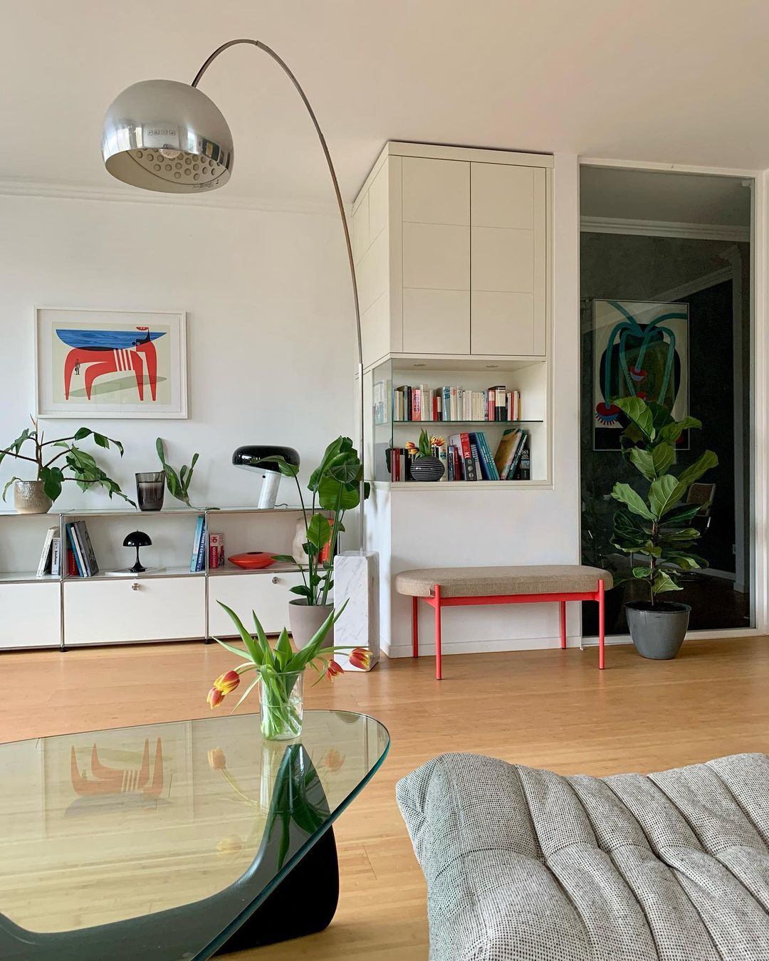 The Clérachic lamp's chrome dome arches over a red bench and fiddle-leaf fig, its marble base beside a low white sideboard.