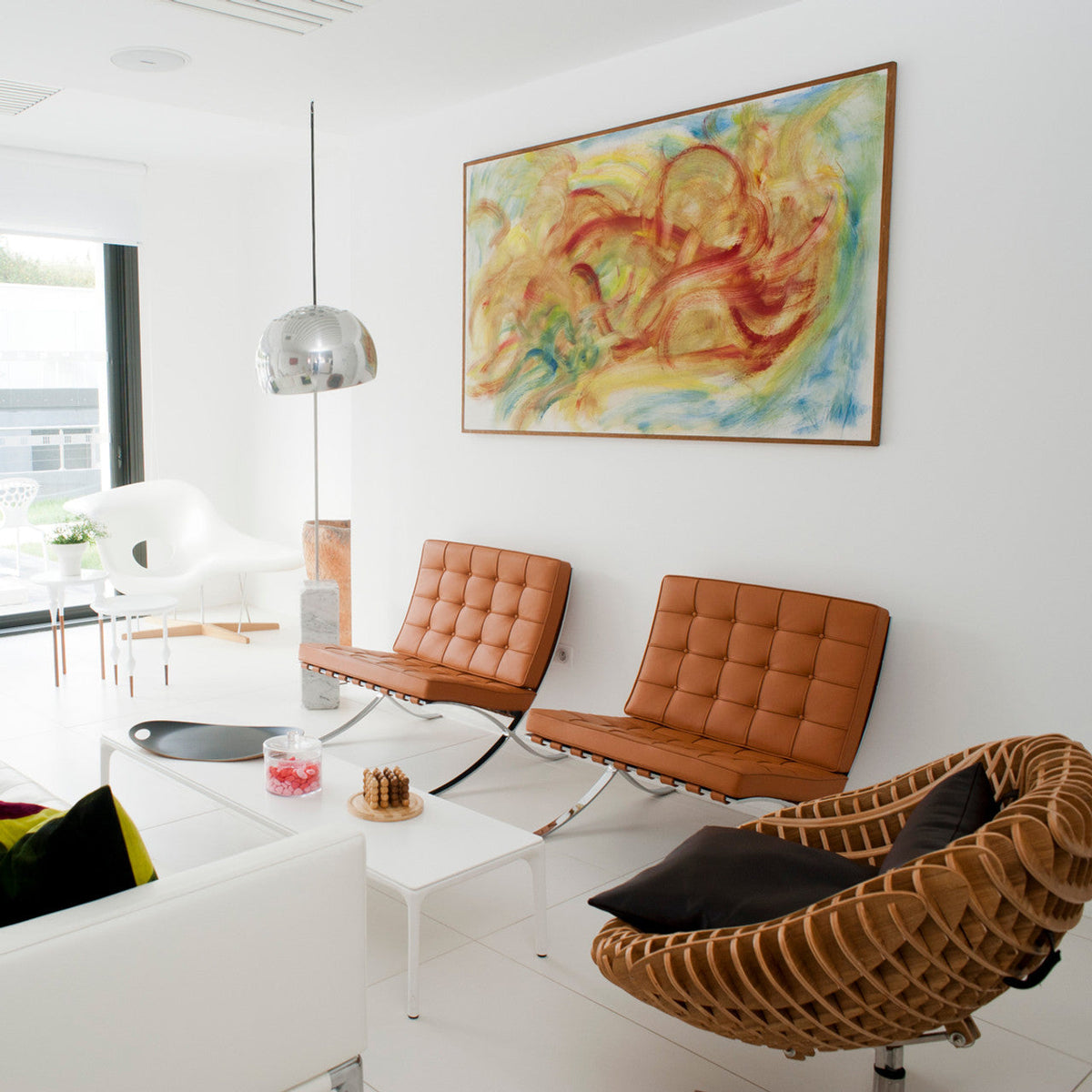 The Clérachic arc lamp's pull-switch chrome dome hangs above tan leather Barcelona-style chairs and a woven cocoon armchair.