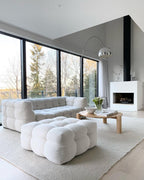The Clérachic arc lamp's marble base stands by a white fireplace, its chrome dome arching over a tufted bouclé sofa and ottoman.