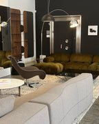 Two arc lamps, one a Clérachic in chrome, curve over a moss-green velvet sofa in a black-walled room with a sculptural chair.