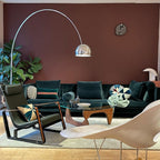 The Clérachic lamp's polished dome arches above a teal velvet sofa and a Noguchi-style coffee table against a rust-coloured wall.