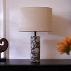 Soft-focused orange and white flowers sit low in the foreground of the Clérachic marble lamp on its dark sideboard.