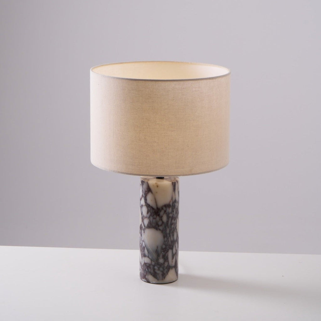 Warmer light glows from the linen shade of the Clérachic marble lamp, set on a plain grey studio background.